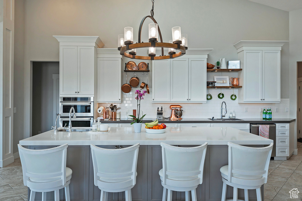 Kitchen with stainless steel appliances, a notable chandelier, sink, tasteful backsplash, and white cabinetry
