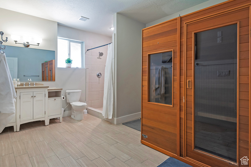 Bathroom featuring curtained shower, a textured ceiling, vanity with extensive cabinet space, and toilet