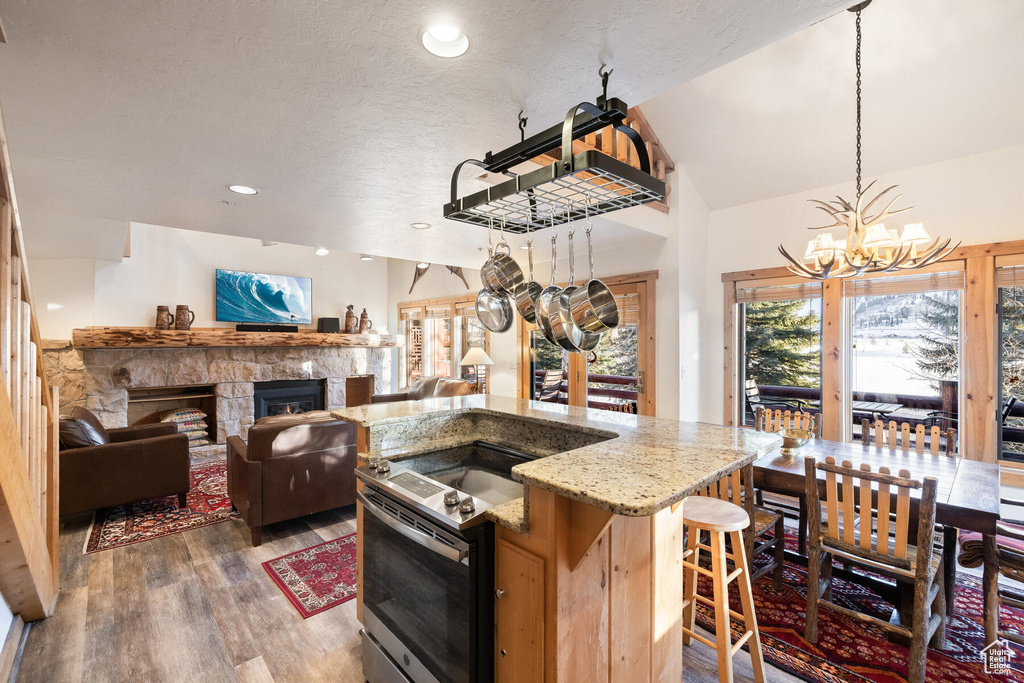 Kitchen featuring a chandelier, a fireplace, light stone countertops, dark hardwood / wood-style flooring, and a kitchen island with sink