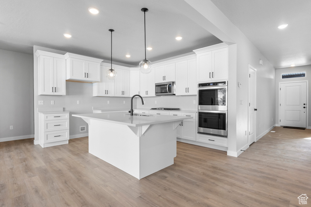 Kitchen featuring white cabinets, appliances with stainless steel finishes, a kitchen island with sink, and light hardwood / wood-style floors