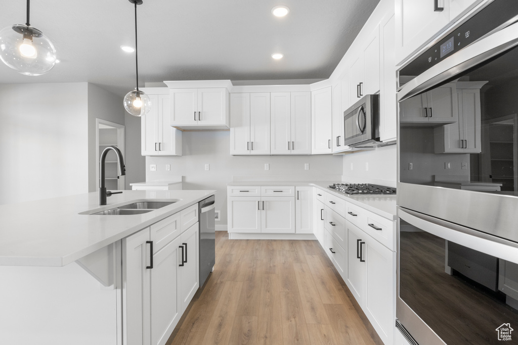 Kitchen featuring white cabinets, light wood-type flooring, stainless steel appliances, pendant lighting, and sink