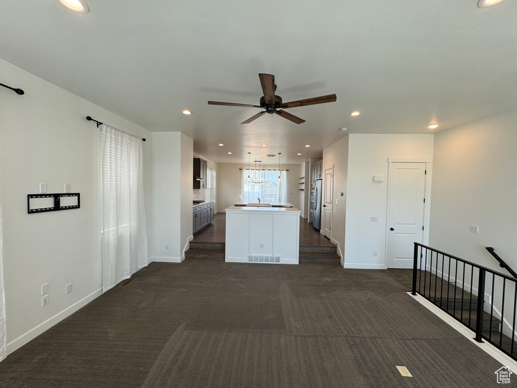 Unfurnished living room with ceiling fan and dark colored carpet
