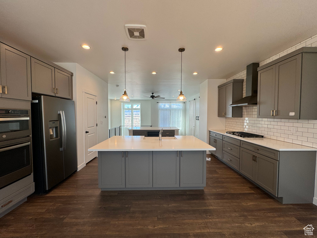 Kitchen with wall chimney range hood, dark hardwood / wood-style flooring, stainless steel appliances, and ceiling fan