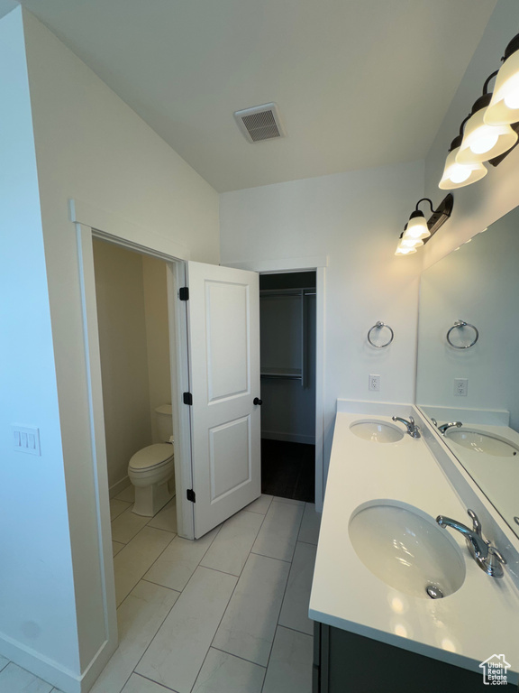 Bathroom featuring tile floors, dual vanity, and toilet