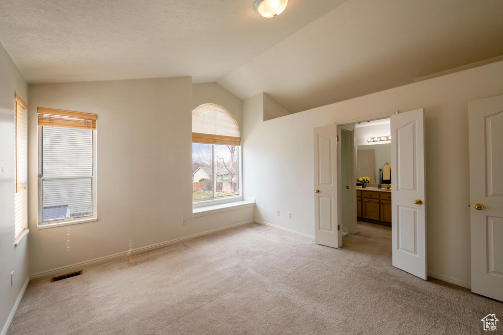 Empty room with vaulted ceiling, light carpet, and a textured ceiling