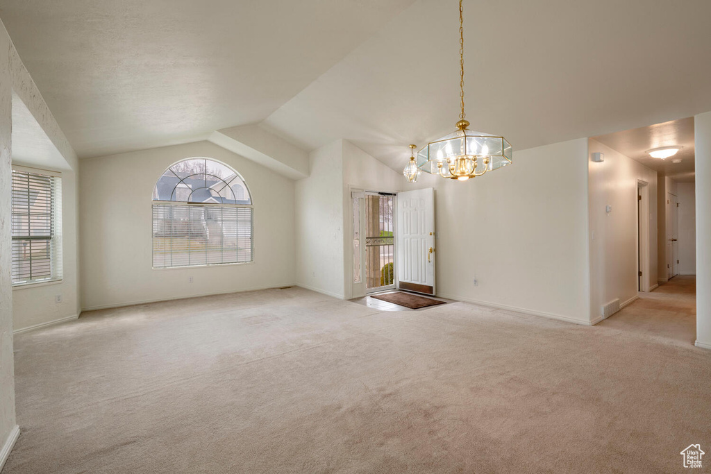 Carpeted empty room with vaulted ceiling and an inviting chandelier