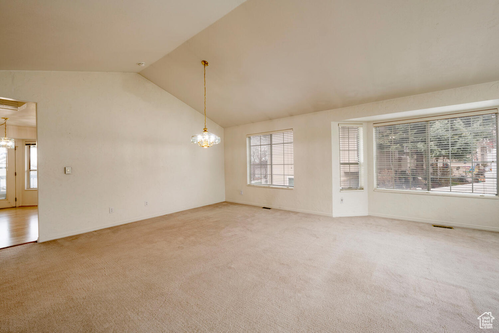 Unfurnished room featuring light colored carpet, high vaulted ceiling, and a chandelier