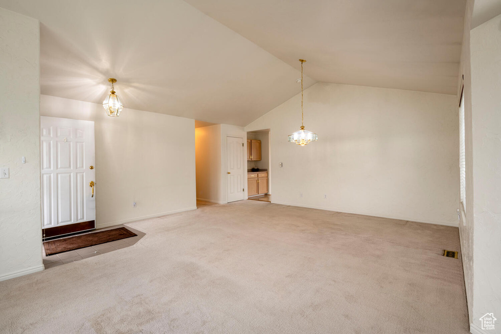 Empty room with light carpet, high vaulted ceiling, and a chandelier