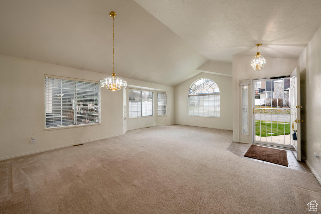 Unfurnished living room featuring light colored carpet, vaulted ceiling, and a notable chandelier