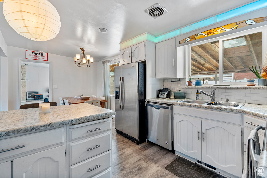 Kitchen with appliances with stainless steel finishes, light hardwood / wood-style floors, decorative light fixtures, backsplash, and a notable chandelier