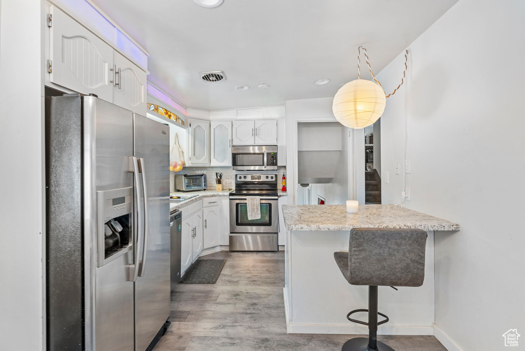Kitchen featuring appliances with stainless steel finishes, hardwood / wood-style floors, light stone countertops, a breakfast bar, and white cabinetry