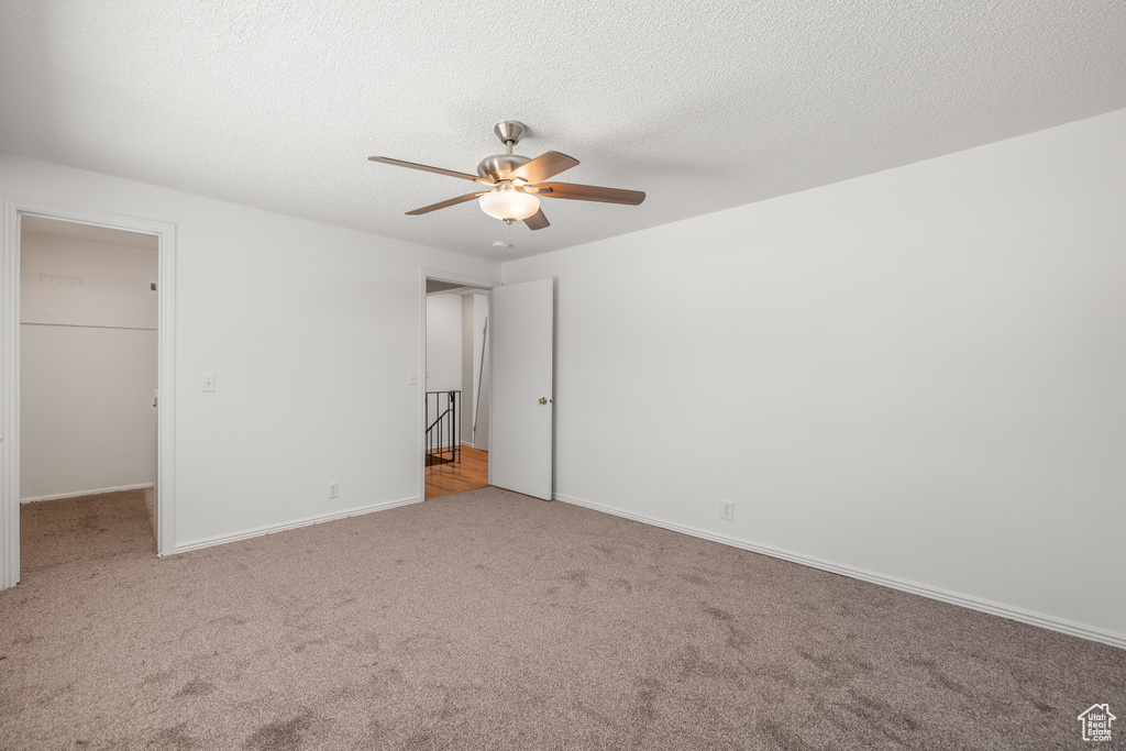 Unfurnished bedroom featuring a walk in closet, a closet, light carpet, and ceiling fan
