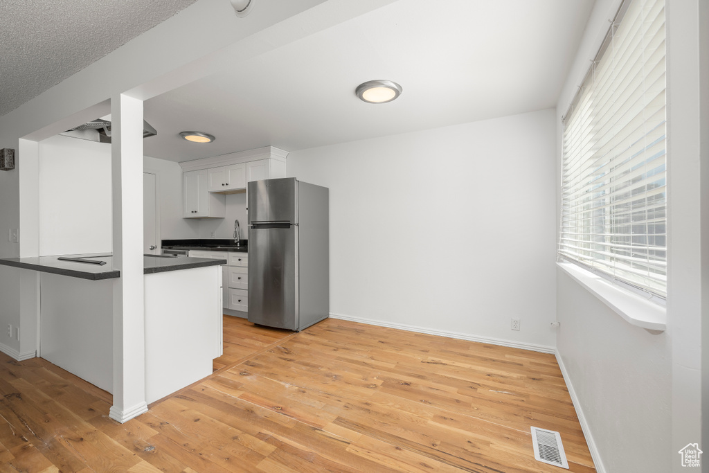 Kitchen with stainless steel refrigerator, plenty of natural light, light wood-type flooring, and white cabinetry