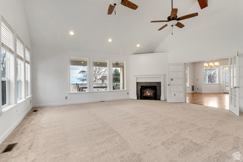 Unfurnished living room featuring ceiling fan with notable chandelier, a healthy amount of sunlight, a tiled fireplace, and light colored carpet