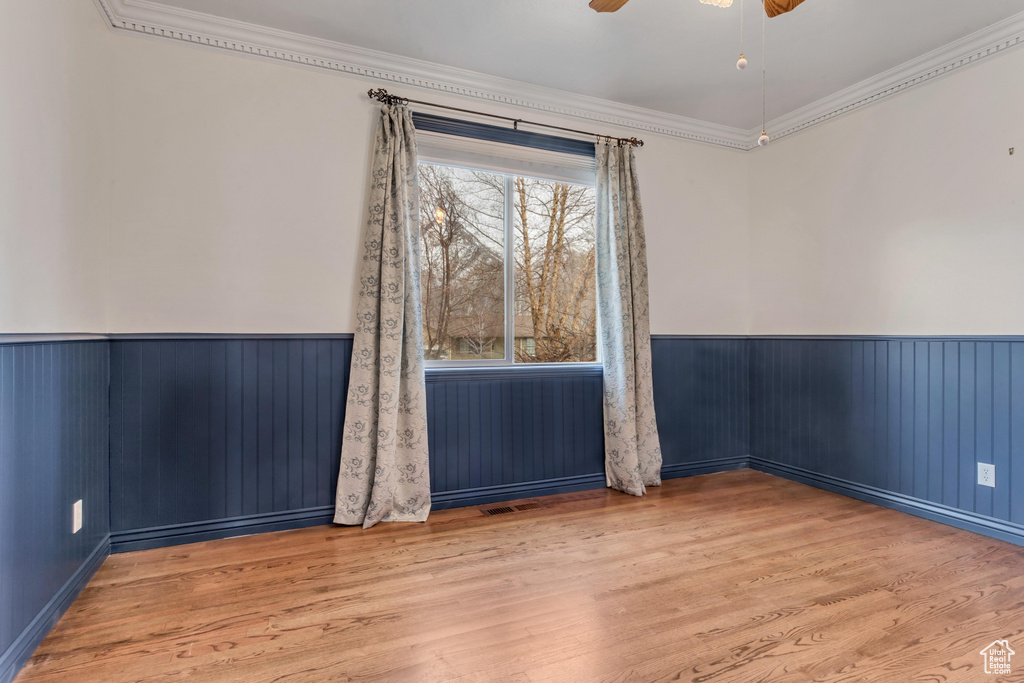Empty room with crown molding, light wood-type flooring, and ceiling fan