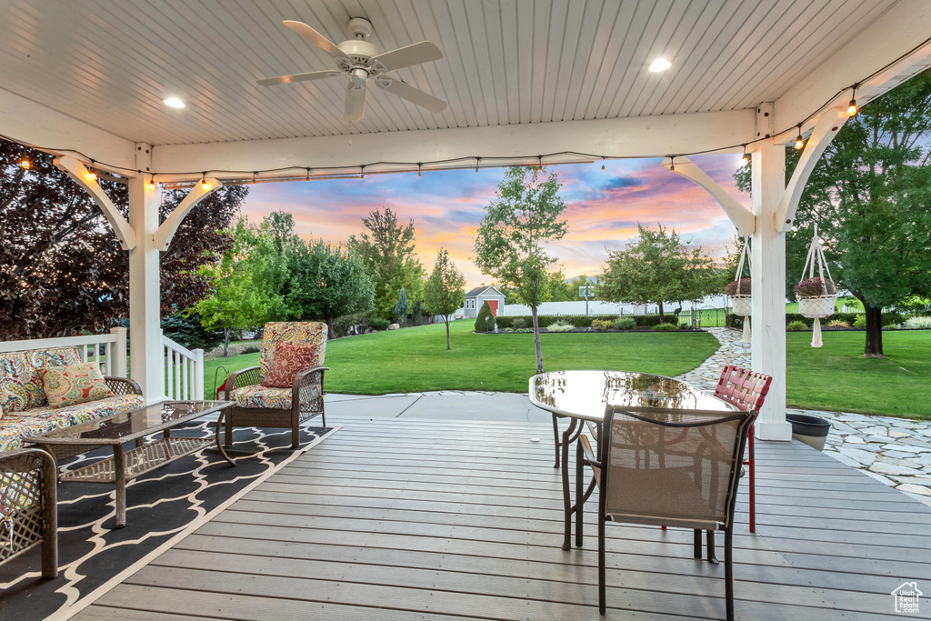 Deck at dusk featuring an outdoor hangout area, a lawn, and ceiling fan