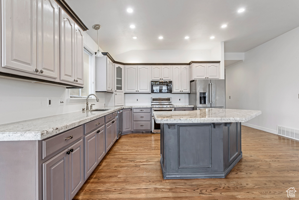 Kitchen with stainless steel appliances, light hardwood / wood-style flooring, sink, decorative light fixtures, and a kitchen island