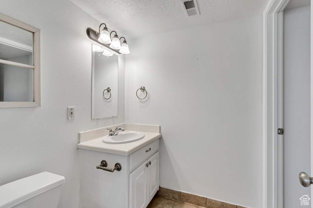 Bathroom with tile flooring, oversized vanity, toilet, and a textured ceiling