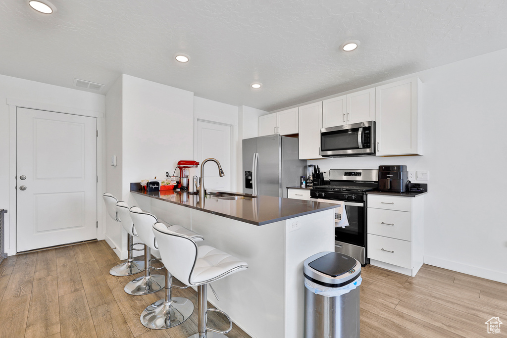 Kitchen featuring a kitchen breakfast bar, stainless steel appliances, light wood-type flooring, and white cabinetry