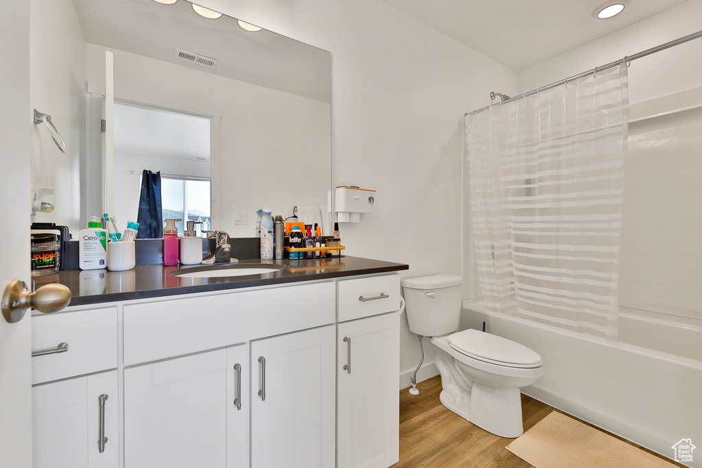 Full bathroom featuring toilet, vanity, shower / bath combo with shower curtain, and hardwood / wood-style flooring