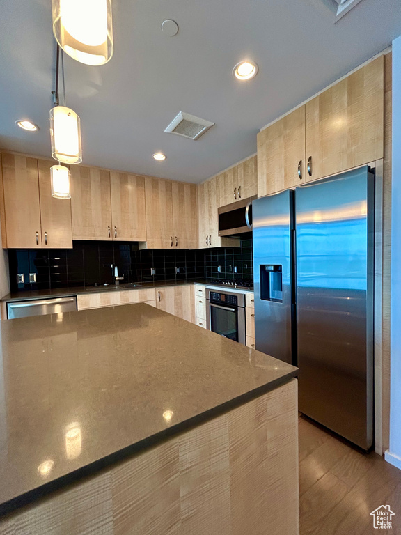 Kitchen featuring pendant lighting, appliances with stainless steel finishes, light hardwood / wood-style floors, light brown cabinetry, and backsplash