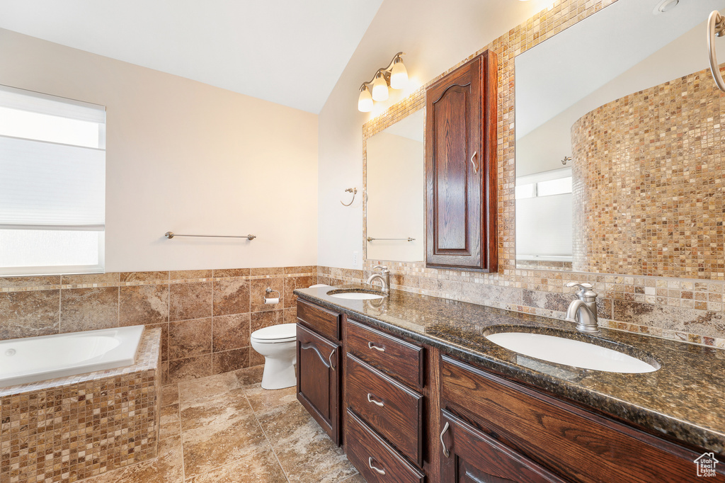 Bathroom with backsplash, tile floors, large vanity, vaulted ceiling, and dual sinks