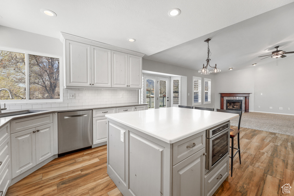 Kitchen with appliances with stainless steel finishes, ceiling fan with notable chandelier, a kitchen island, light hardwood / wood-style flooring, and white cabinetry