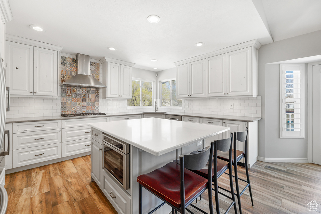 Kitchen with wall chimney range hood, white cabinets, and light hardwood / wood-style floors