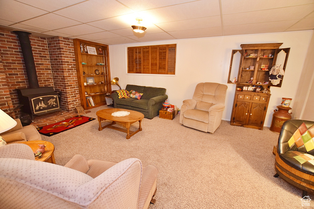 Carpeted living room featuring a paneled ceiling, brick wall, and a wood stove