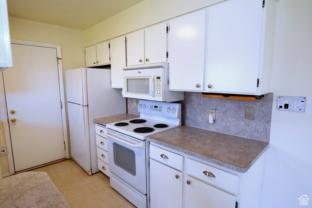 Kitchen featuring white cabinets, white appliances, light tile flooring, and backsplash