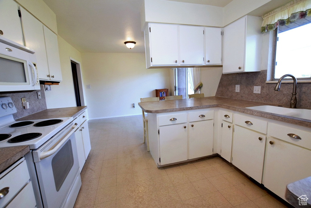 Kitchen featuring white appliances, backsplash, light tile floors, kitchen peninsula, and white cabinetry