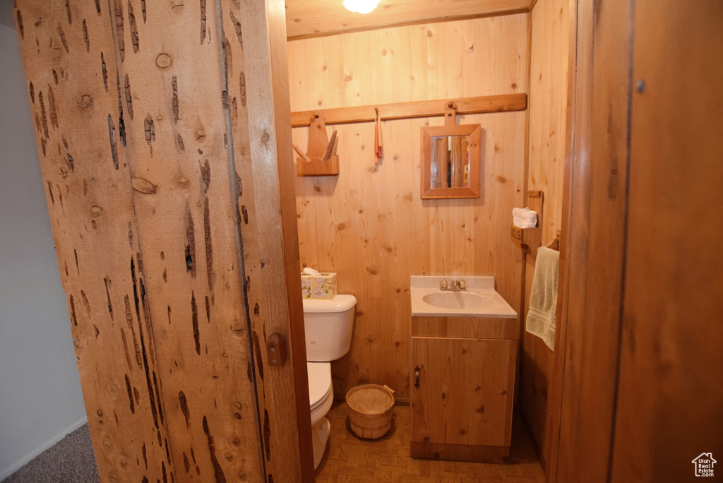 Bathroom with parquet flooring, vanity, wooden walls, and toilet