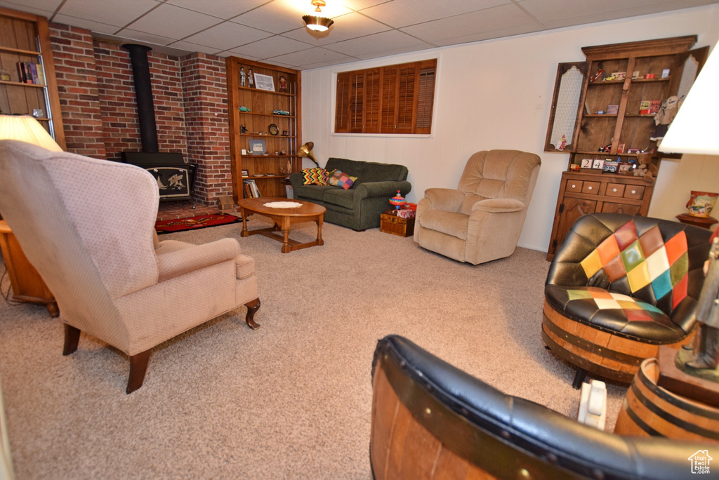 Carpeted living room with a paneled ceiling, built in features, brick wall, and a wood stove