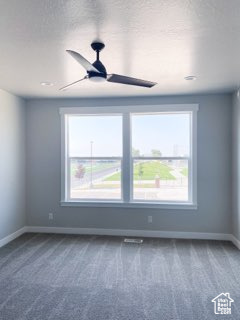 Spare room with dark colored carpet, ceiling fan, and a wealth of natural light
