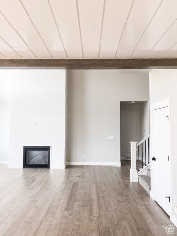 Unfurnished room featuring a fireplace, beam ceiling, and dark hardwood / wood-style flooring