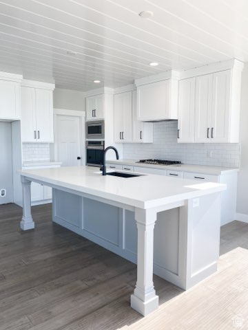 Kitchen featuring stainless steel appliances, a center island with sink, and white cabinetry