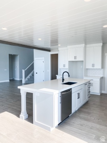 Kitchen with sink, a kitchen island with sink, white cabinets, and stainless steel dishwasher