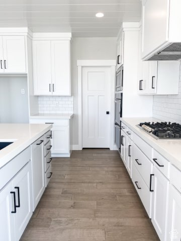 Kitchen featuring tasteful backsplash, white cabinets, light hardwood / wood-style floors, and custom range hood