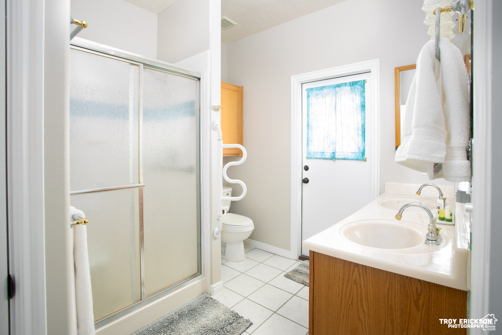 Bathroom featuring a shower with shower door, tile floors, vanity, and toilet