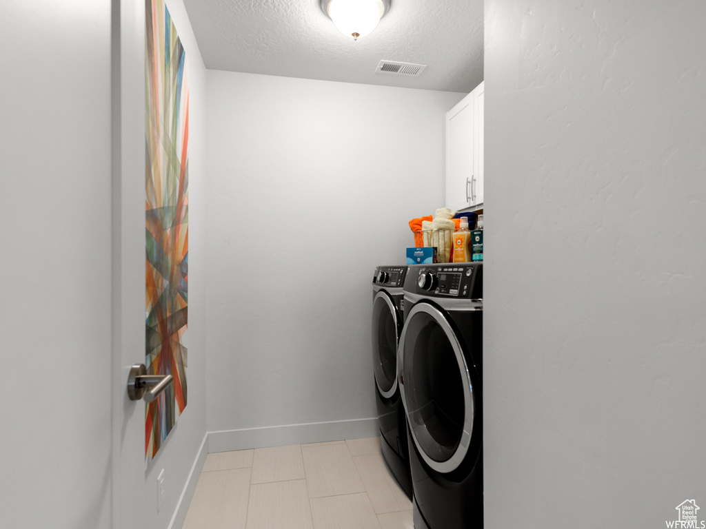 Laundry area featuring washer and dryer, a textured ceiling, light tile floors, and cabinets