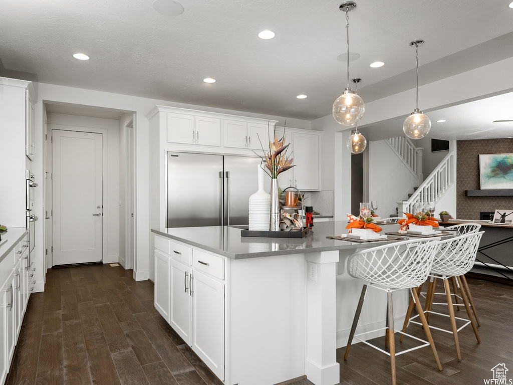 Kitchen with pendant lighting, stainless steel built in fridge, dark hardwood / wood-style floors, a center island with sink, and white cabinetry