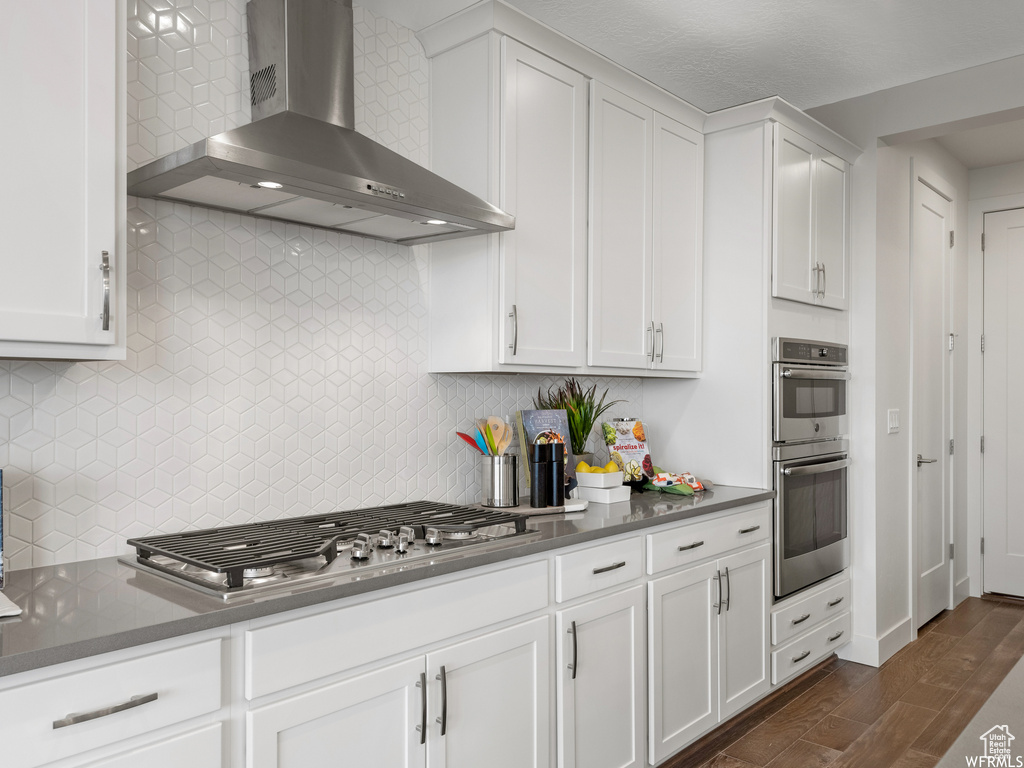 Kitchen with dark hardwood / wood-style flooring, wall chimney range hood, backsplash, and stainless steel appliances