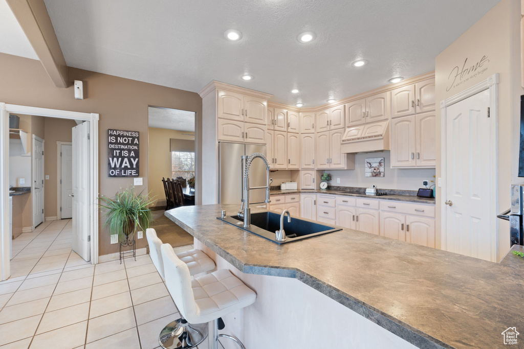 Kitchen with a kitchen bar, sink, premium range hood, high quality fridge, and light tile floors