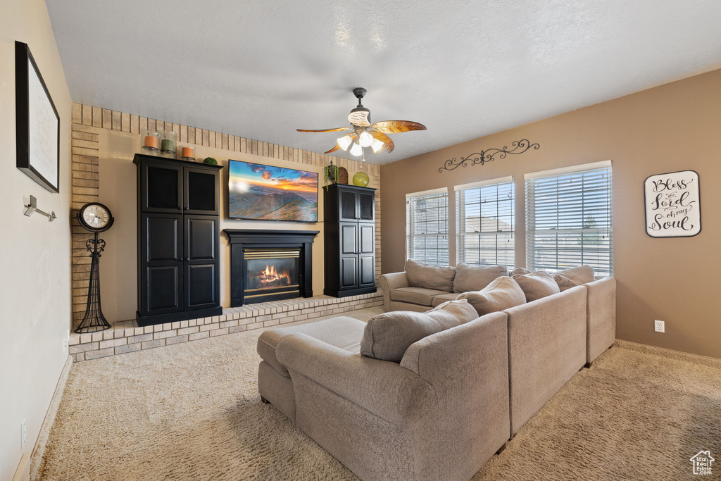 Living room with a brick fireplace, light colored carpet, and ceiling fan