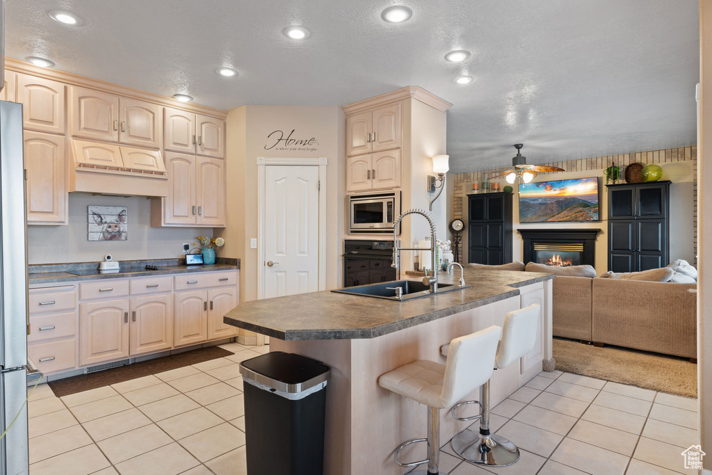 Kitchen featuring stainless steel appliances, light tile floors, ceiling fan, a center island with sink, and sink