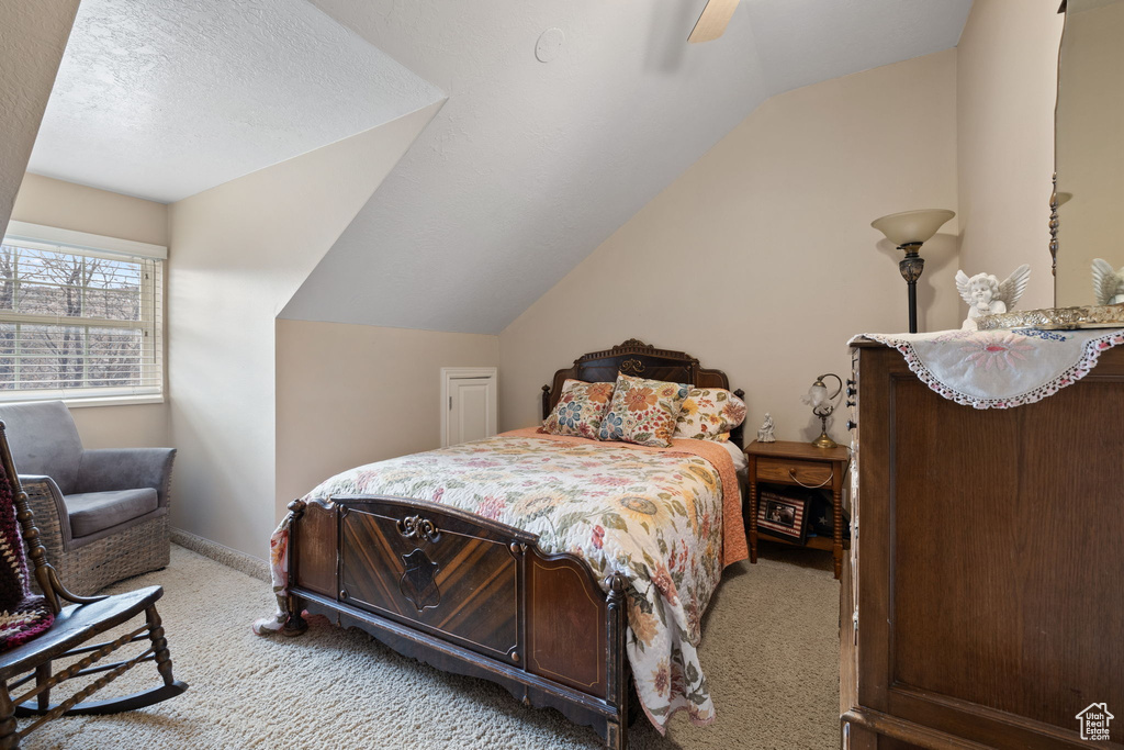 Carpeted bedroom featuring vaulted ceiling, ceiling fan, and a textured ceiling
