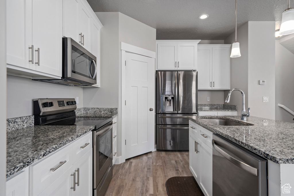 Kitchen featuring white cabinets, hardwood / wood-style flooring, sink, appliances with stainless steel finishes, and hanging light fixtures