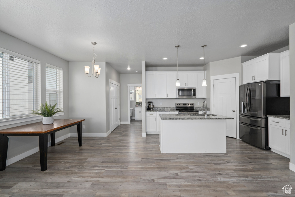 Kitchen featuring appliances with stainless steel finishes, pendant lighting, a notable chandelier, and hardwood / wood-style floors