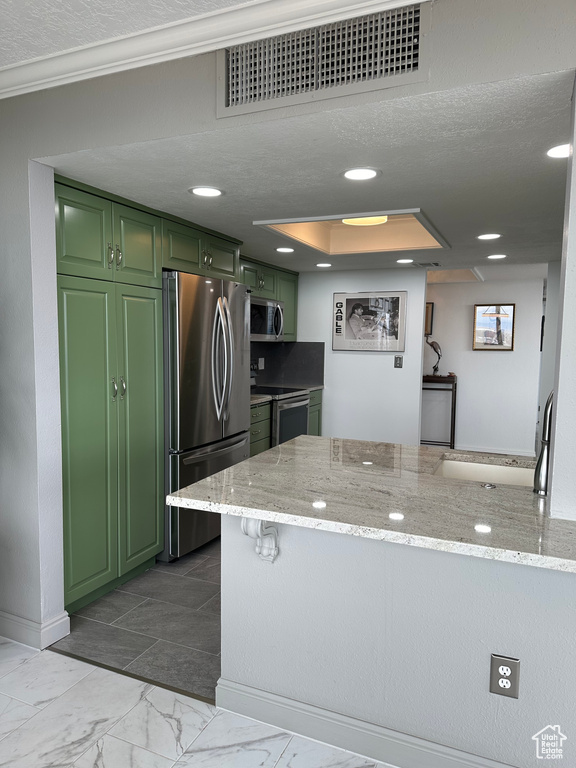 Kitchen with appliances with stainless steel finishes, light stone counters, light tile flooring, and green cabinets