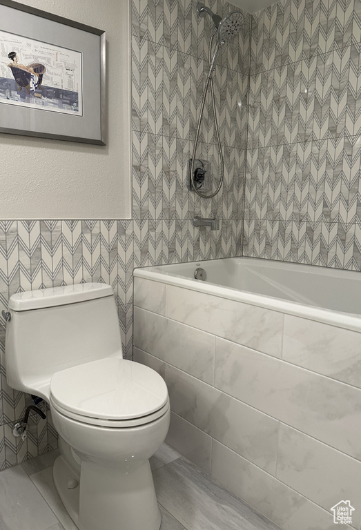 Bathroom featuring tile walls, tile flooring, tiled shower / bath, and toilet